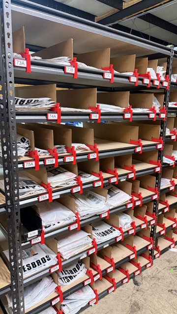 Real warehouse installation — Easy Shelf Dividers organizing apparel mailers across five shelf rows